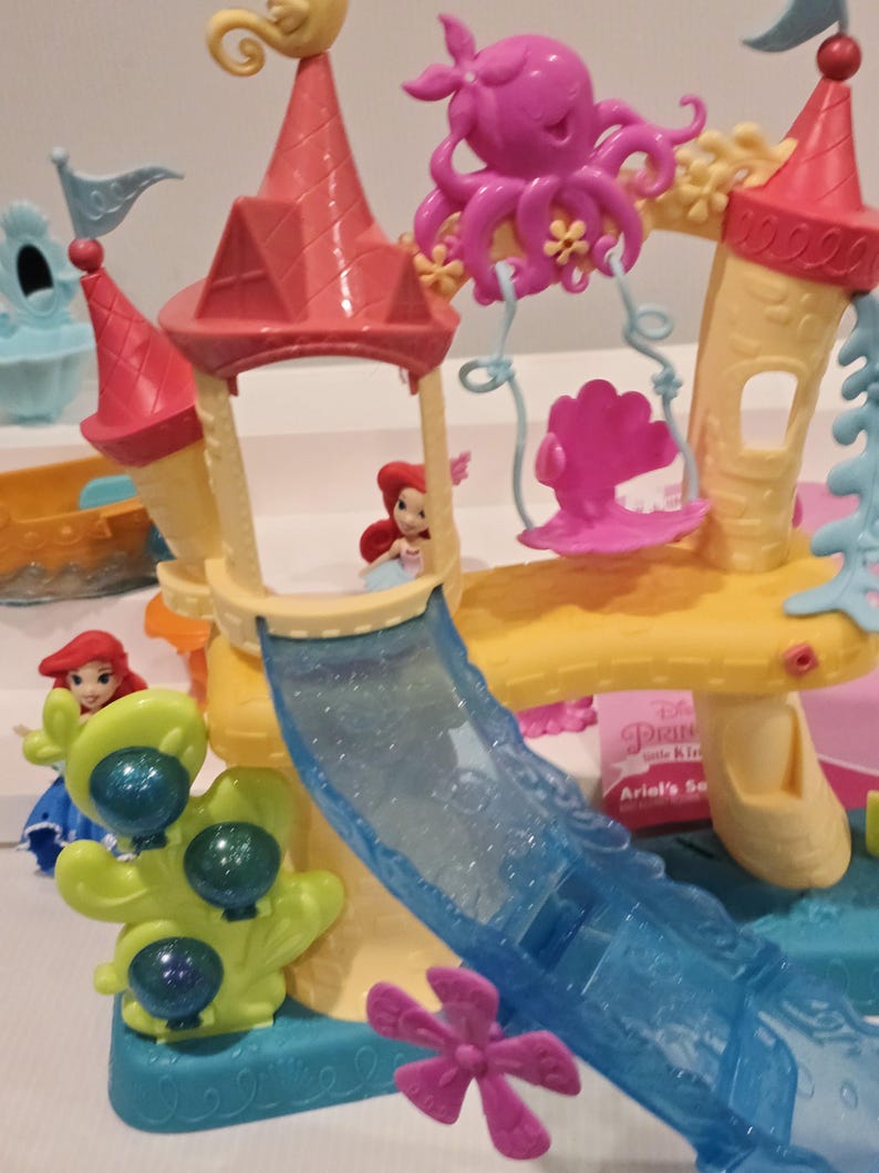 K&ouml;nnte beinhalten: Ariel's Secret Spielset mit einem gelben und rosa Schloss mit einer blauen Rutsche, einem rosa Oktopus und einer rosa Muschelschaukel. Das Set enth&auml;lt eine kleine Ariel-Figur. F&uuml;r Kinder konzipiert.