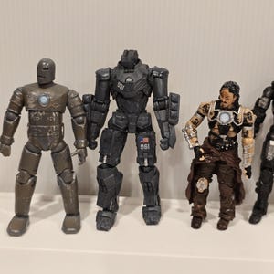 May include: A collection of action figures featuring characters in various poses. The figures are primarily in shades of gray, brown, and black, with some metallic accents. The figures appear to be from a science fiction or superhero genre.
