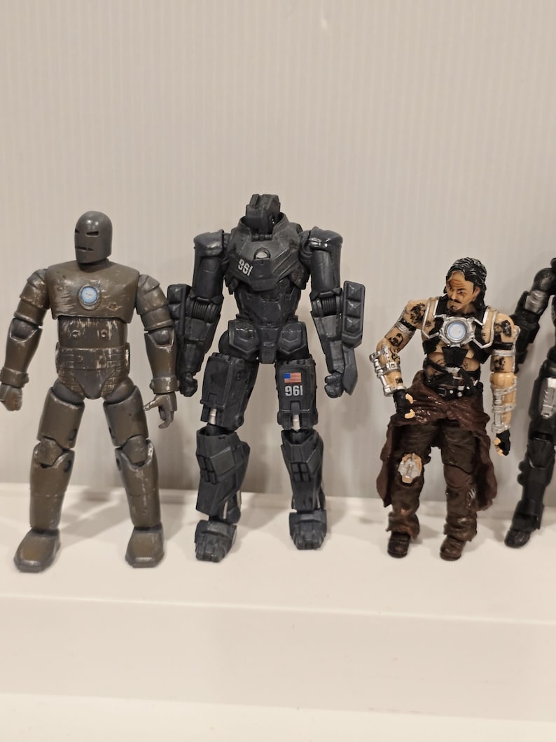 May include: A collection of action figures featuring characters in various poses. The figures are primarily in shades of gray, brown, and black, with some metallic accents. The figures appear to be from a science fiction or superhero genre.
