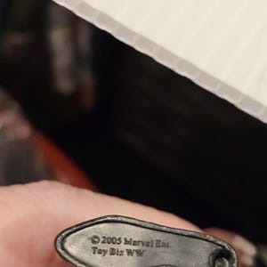 May include: A close-up of the base of a black action figure. The base is dark gray and has the text "&copy; 2005 Marvel Ent. Toy Biz WW" printed on it.