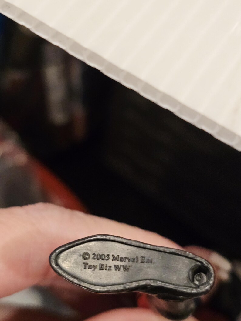 May include: A close-up of the base of a black action figure. The base is dark gray and has the text "&copy; 2005 Marvel Ent. Toy Biz WW" printed on it.