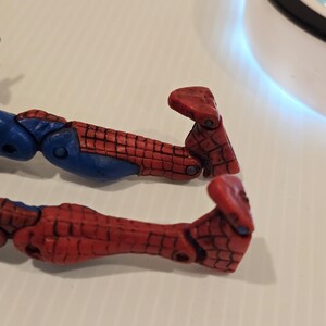 Pode incluir: Close-up de duas pernas de boneco de a&ccedil;&atilde;o vermelhas e azuis. As pernas apresentam um padr&atilde;o de teia de aranha vermelha e detalhes azuis. Os p&eacute;s s&atilde;o de uma tonalidade mais escura de vermelho.