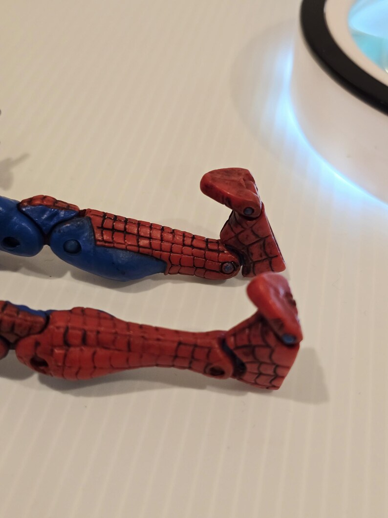 Pode incluir: Close-up de duas pernas de boneco de a&ccedil;&atilde;o vermelhas e azuis. As pernas apresentam um padr&atilde;o de teia de aranha vermelha e detalhes azuis. Os p&eacute;s s&atilde;o de uma tonalidade mais escura de vermelho.