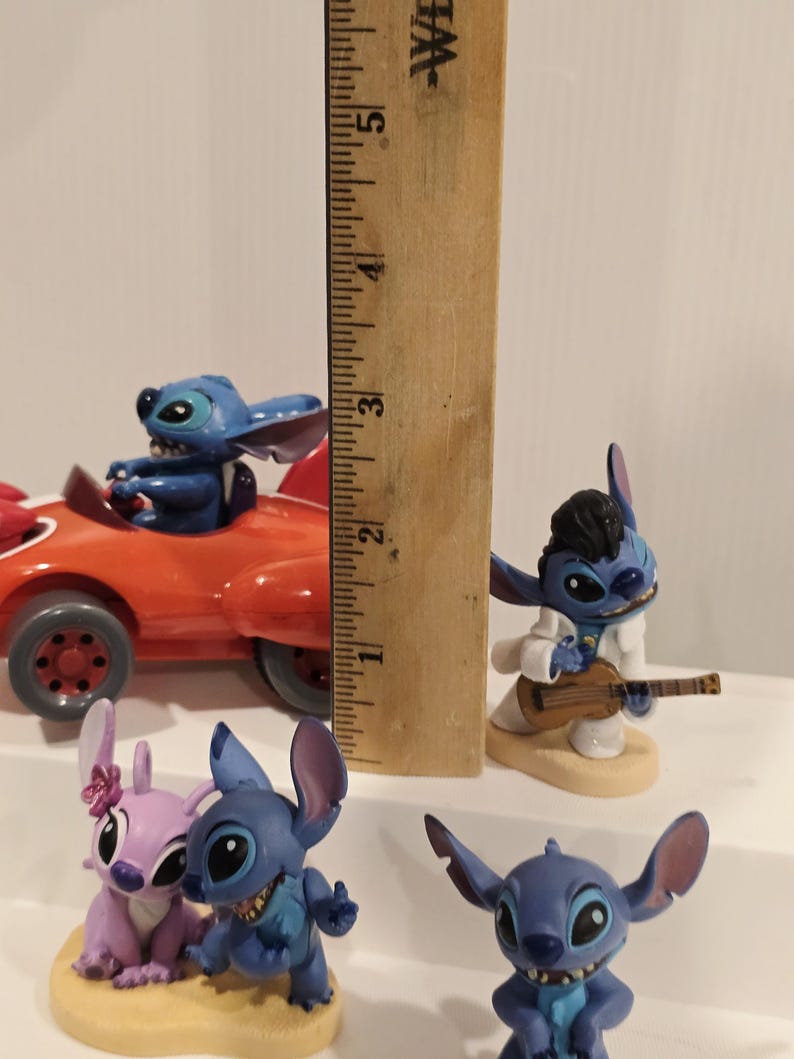 May include: A collection of Stitch figurines, including one in a red car, one playing a guitar, and others in various poses. The tallest figurine measures approximately 5 inches.