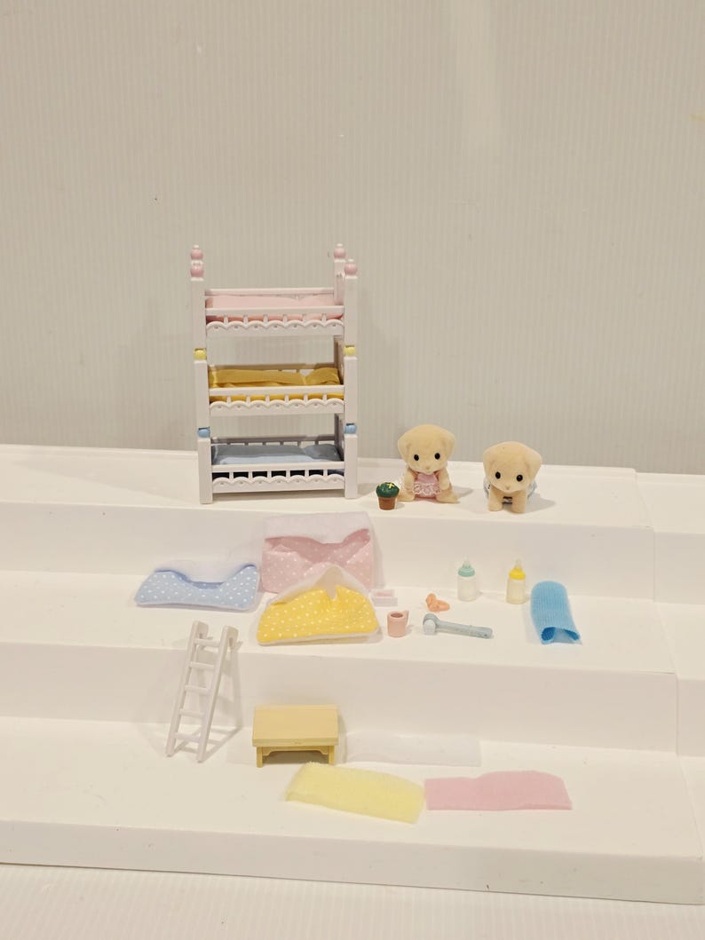 Puede incluir: Un juego de dormitorio de casa de mu&ntilde;ecas en miniatura con una litera, dos cachorros de juguete y varios accesorios. La litera tiene ropa de cama rosa, amarilla y azul. Los accesorios incluyen una escalera, una mesa, mantas, biberones y un martillo de juguete.