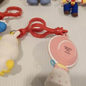 May include: A selection of Toy Story character keyrings. The keyrings feature characters such as Bo Peep, Mr. Potato Head, and Woody. The keyrings are made of plastic and have red plastic clips.