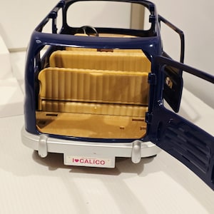 May include: A navy blue toy car with open doors, revealing tan seating. The car has a silver bumper and a license plate that reads "I ❤️ CALICO". The steering wheel is visible inside the car.
