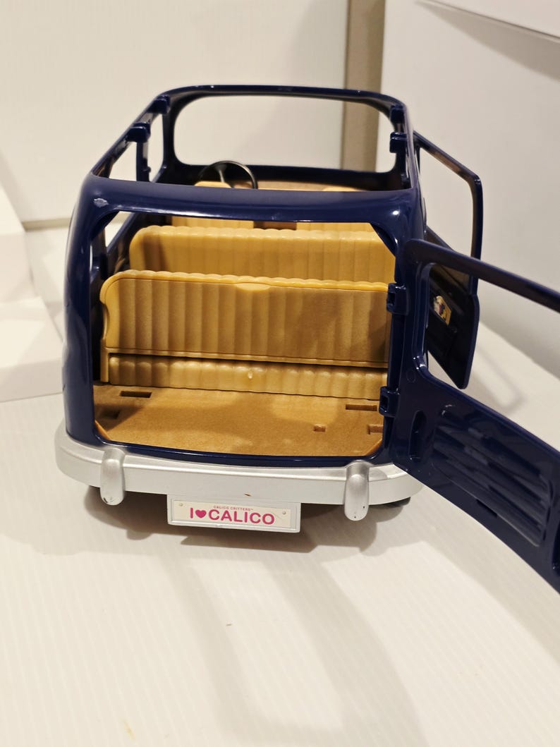 May include: A navy blue toy car with open doors, revealing tan seating. The car has a silver bumper and a license plate that reads "I ❤️ CALICO". The steering wheel is visible inside the car.