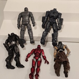 May include: Six action figures are arranged on a white surface. The figures include a metallic gray robot, a red and silver figure, and several black figures with varying armor designs. The figures are detailed and appear to be from a science fiction or superhero theme.