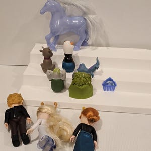 May include: A collection of toy figures from the animated movie "Frozen." The set includes a light purple horse, a reindeer, a snowman, and three dolls. The dolls have blonde and red hair, and are wearing various outfits.