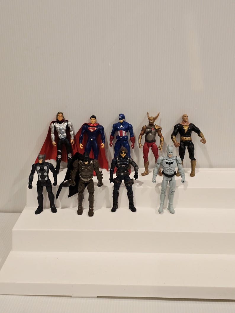 May include: A collection of ten superhero action figures, each with unique costumes and poses. The figures are displayed on a white tiered platform against a plain white background. The figures include Superman, Batman, and Captain America.