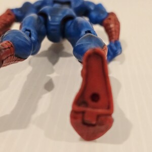 Pode incluir: Uma figura de a&ccedil;&atilde;o azul e vermelha de um super-her&oacute;i, deitada de costas. A figura tem um corpo azul com detalhes vermelhos nos bra&ccedil;os e p&eacute;s. A figura &eacute; articulada e parece ser de pl&aacute;stico.
