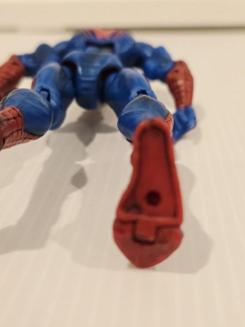 Pode incluir: Uma figura de a&ccedil;&atilde;o azul e vermelha de um super-her&oacute;i, deitada de costas. A figura tem um corpo azul com detalhes vermelhos nos bra&ccedil;os e p&eacute;s. A figura &eacute; articulada e parece ser de pl&aacute;stico.