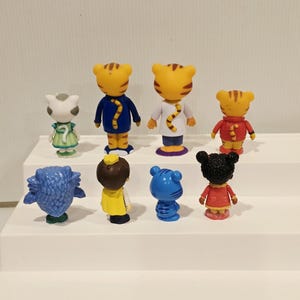 May include: A collection of eight small plastic character figurines arranged in two rows. The figures include various anthropomorphic animals and children, all viewed from the back, showcasing their colorful outfits, tails, and distinct hairstyles.