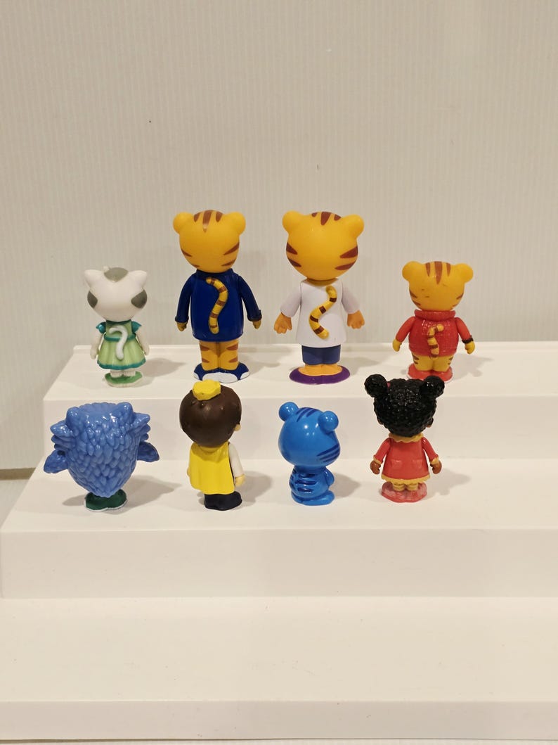 May include: A collection of eight small plastic character figurines arranged in two rows. The figures include various anthropomorphic animals and children, all viewed from the back, showcasing their colorful outfits, tails, and distinct hairstyles.