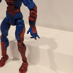 Pode incluir: Figura de a&ccedil;&atilde;o azul e vermelha do Homem-Aranha. A figura tem um design detalhado com um padr&atilde;o de teia nas se&ccedil;&otilde;es vermelhas. A figura est&aacute; em pose com um bra&ccedil;o estendido.