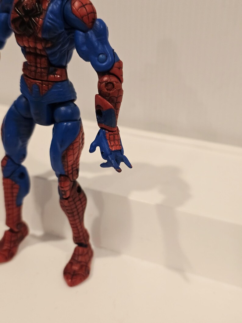 Pode incluir: Figura de a&ccedil;&atilde;o azul e vermelha do Homem-Aranha. A figura tem um design detalhado com um padr&atilde;o de teia nas se&ccedil;&otilde;es vermelhas. A figura est&aacute; em pose com um bra&ccedil;o estendido.