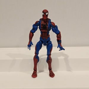 Pode incluir: Uma figura de a&ccedil;&atilde;o do Homem-Aranha em pose de p&eacute;. A figura &eacute; principalmente vermelha e azul, com um emblema de aranha preta no peito. Design detalhado, com m&uacute;sculos vis&iacute;veis e uma m&aacute;scara cl&aacute;ssica do Homem-Aranha.