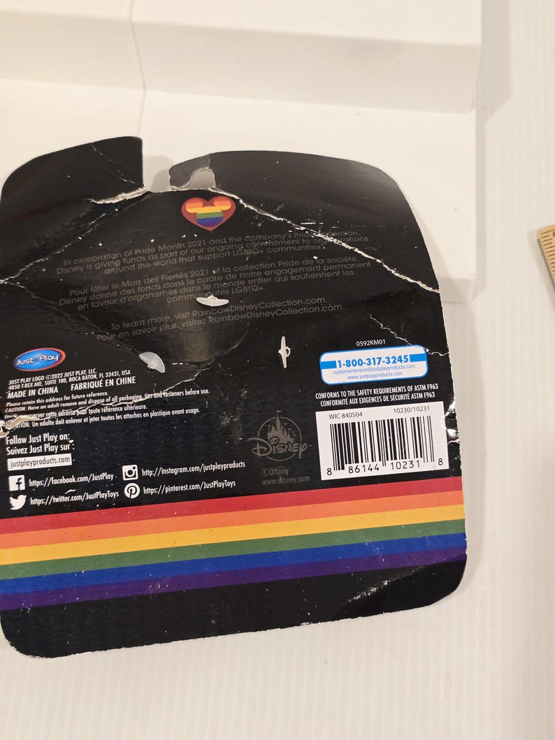 May include: A black product package with a rainbow-colored stripe at the bottom. The package has text and logos, including the Disney logo and a heart-shaped emblem with a rainbow design. The package is slightly torn.