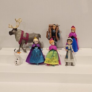 May include: A collection of Frozen-themed figurines. The set includes characters like Anna, Elsa, Kristoff, and Olaf, along with a reindeer. The figurines are brightly colored and detailed, with a focus on the characters' outfits and accessories.