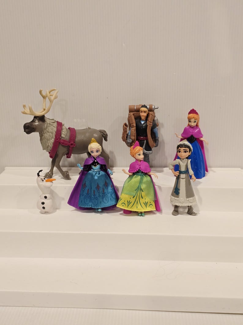 May include: A collection of Frozen-themed figurines. The set includes characters like Anna, Elsa, Kristoff, and Olaf, along with a reindeer. The figurines are brightly colored and detailed, with a focus on the characters' outfits and accessories.