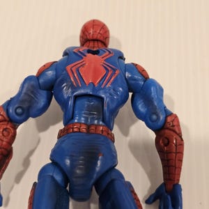 Pode incluir: Figura de a&ccedil;&atilde;o azul e vermelha de um super-her&oacute;i, vista por tr&aacute;s. A figura tem um emblema de aranha vermelho nas costas e detalhes vermelhos nos bra&ccedil;os e pernas. A cabe&ccedil;a &eacute; vermelha com um padr&atilde;o de teia.