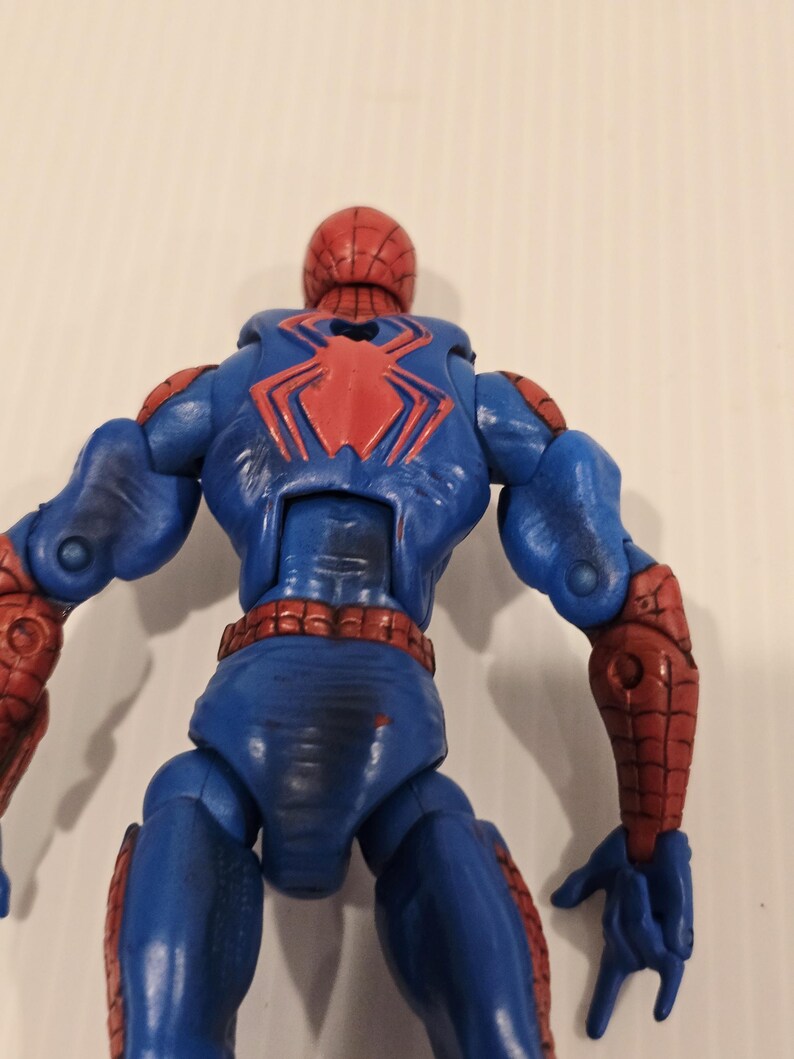 Pode incluir: Figura de a&ccedil;&atilde;o azul e vermelha de um super-her&oacute;i, vista por tr&aacute;s. A figura tem um emblema de aranha vermelho nas costas e detalhes vermelhos nos bra&ccedil;os e pernas. A cabe&ccedil;a &eacute; vermelha com um padr&atilde;o de teia.