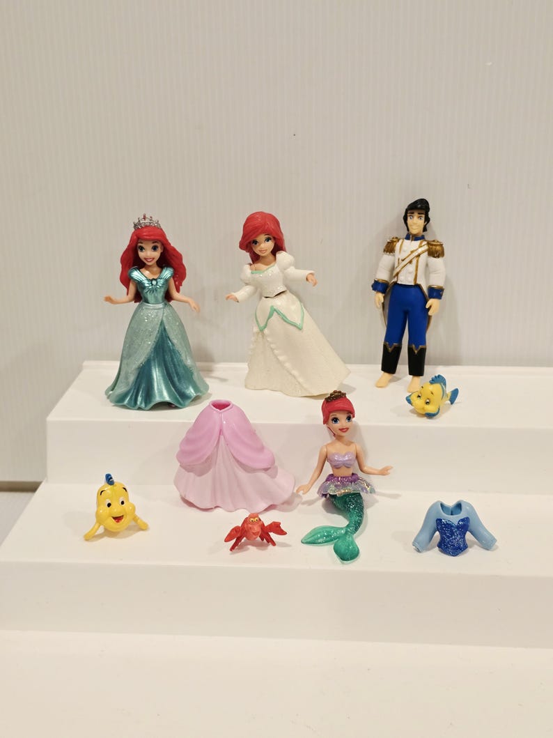 K&ouml;nnte beinhalten: Eine Sammlung von Disney's Die kleine Meerjungfrau Figuren. Das Set enth&auml;lt Arielle in einem t&uuml;rkisfarbenen Kleid, Arielle in einem wei&szlig;en Kleid, Prinz Eric, Fabius, ein rosa Kleid, Sebastian, eine Meerjungfrau Arielle und ein blaues Oberteil.
