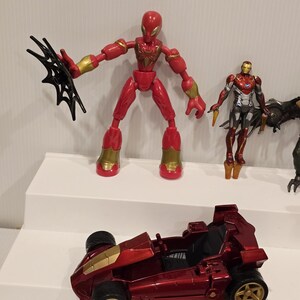 May include: A collection of red and gold action figures and a red race car toy. The Spider-Man figure is red with gold accents and a black web accessory. The race car is red with gold wheels.