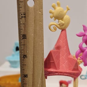 K&ouml;nnte beinhalten: Ein Miniatur-Spielset mit einer rosa burg&auml;hnlichen Struktur mit einer gelben Seepferdchenfigur oben. Das Spielset enth&auml;lt eine kleine Ariel-Figur. Das Spielset ist etwa 25 cm hoch.