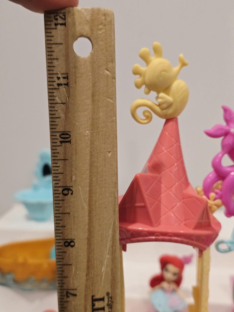 K&ouml;nnte beinhalten: Ein Miniatur-Spielset mit einer rosa burg&auml;hnlichen Struktur mit einer gelben Seepferdchenfigur oben. Das Spielset enth&auml;lt eine kleine Ariel-Figur. Das Spielset ist etwa 25 cm hoch.