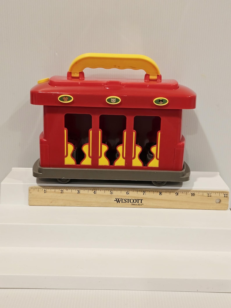 K&ouml;nnte beinhalten: Ein roter Spielzeugzug mit gelbem Griff und R&auml;dern. Der Zug hat drei &Ouml;ffnungen mit gelben gitarrenf&ouml;rmigen Ausschnitten. Der Zug ist etwa 30 cm lang.