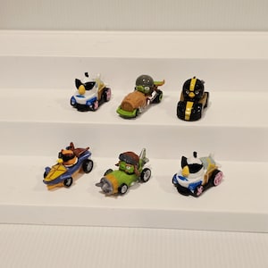 May include: A collection of six miniature toy cars featuring characters from the Angry Birds franchise. Each car has a unique design, with vibrant colors and character-specific details. The cars are displayed on a white surface.
