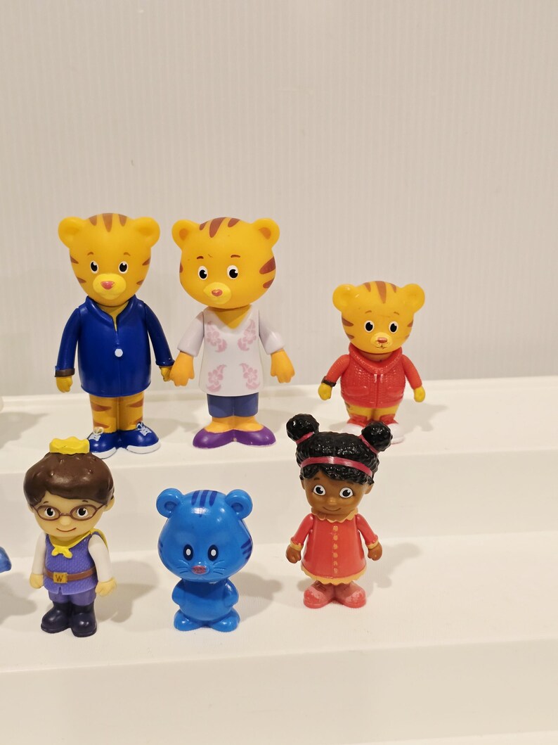 May include: A collection of six small plastic character figurines. The set includes two yellow tiger figures, one smaller yellow tiger, a figure with brown hair and glasses, a small blue cat-like figure, and a figure with dark hair in buns.