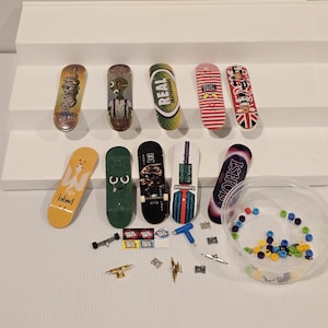 May include: A collection of miniature skateboards in various designs, including a snake, an alien, and a Real Skateboards logo. Also includes small skateboard parts and a container of colorful wheels. The skateboards are displayed on a white surface.