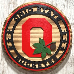 May include: A wooden round sign with a red "O" in the center, surrounded by a black circle with the text "Ohio State Buckeyes" and a green buckeye leaf.