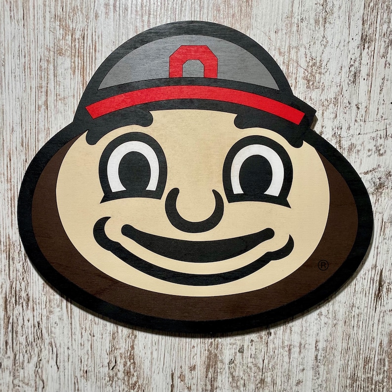 May include: A brown and tan cartoon face with a red and gray hat. The face has a big smile and large eyes. The hat has a white letter "O" on it.