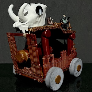 Könnte beinhalten: Ein Miniatur-Holzkarren mit einem weißen Schädel oben, zwei Figuren hinten und braunen Rädern. Der Karren ist aus braunem Holz und hat eine rote Basis.