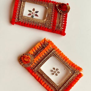 May include: Two decorative frames with gold trim and red and orange fringe. The frames have clear plastic inserts and are decorated with rhinestones.