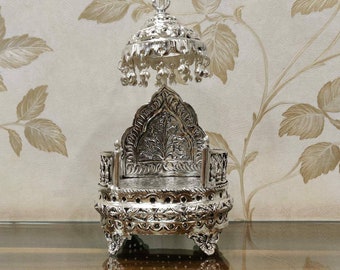 May include: A silver throne with intricate carvings and a dome-shaped canopy. The throne is decorated with floral patterns and has a round base.
