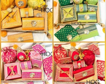 Op de afbeelding: Vier schalen met verschillende decoratieve items in verschillende kleuren. De schalen zijn gevuld met kleine zakjes, dozen en andere items. De kleuren zijn geel, groen, roze en rood.