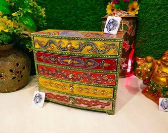 Könnte beinhalten: Eine Holzkiste mit fünf Schubladen, die mit bunten Blumenmustern bemalt sind. Die Kiste ist mit goldenen Akzenten verziert und hat eine abgerundete Vorderseite.