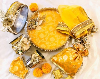 Könnte beinhalten: Ein dekoratives Tablett in Gelb und Gold mit einem Blumenmuster, umgeben von verschiedenen Gegenständen wie einer kleinen Tasche, einer Tasse, einer kleinen Schale und einem dekorativen Stirnband.