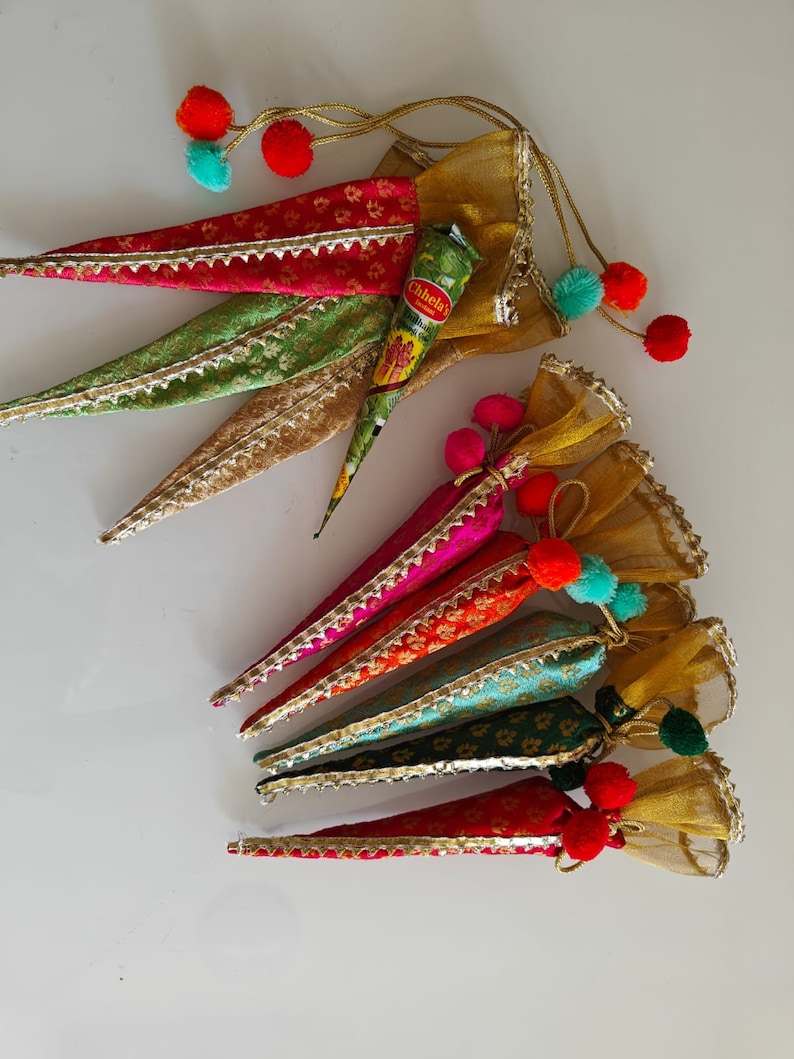 May include: A set of six colorful henna cones, each wrapped in a decorative fabric pouch with a tassel. The pouches are in shades of gold, green, pink, orange, and blue. The cones are ready for use in traditional henna art.
