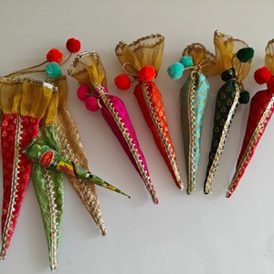 May include: Six colorful cone-shaped pouches with gold trim and pom-poms, filled with henna cones. The pouches are made of sheer fabric with a floral pattern. The henna cones are labeled "Mehndi's".
