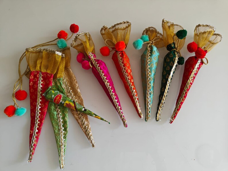 May include: Six colorful cone-shaped pouches with gold trim and pom-poms, filled with henna cones. The pouches are made of sheer fabric with a floral pattern. The henna cones are labeled "Mehndi's".