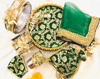 Op de afbeelding: Een groene en gouden decoratieve schaal met een bloemenpatroon, een groene, doorschijnende sjaal met gouden rand en een klein groen en gouden tasje. De schaal is omringd door kleine decoratieve items, waaronder een ronde zilveren container met een gouden rand, een klein glazen kopje met een gouden rand en een klein groen en gouden tasje.
