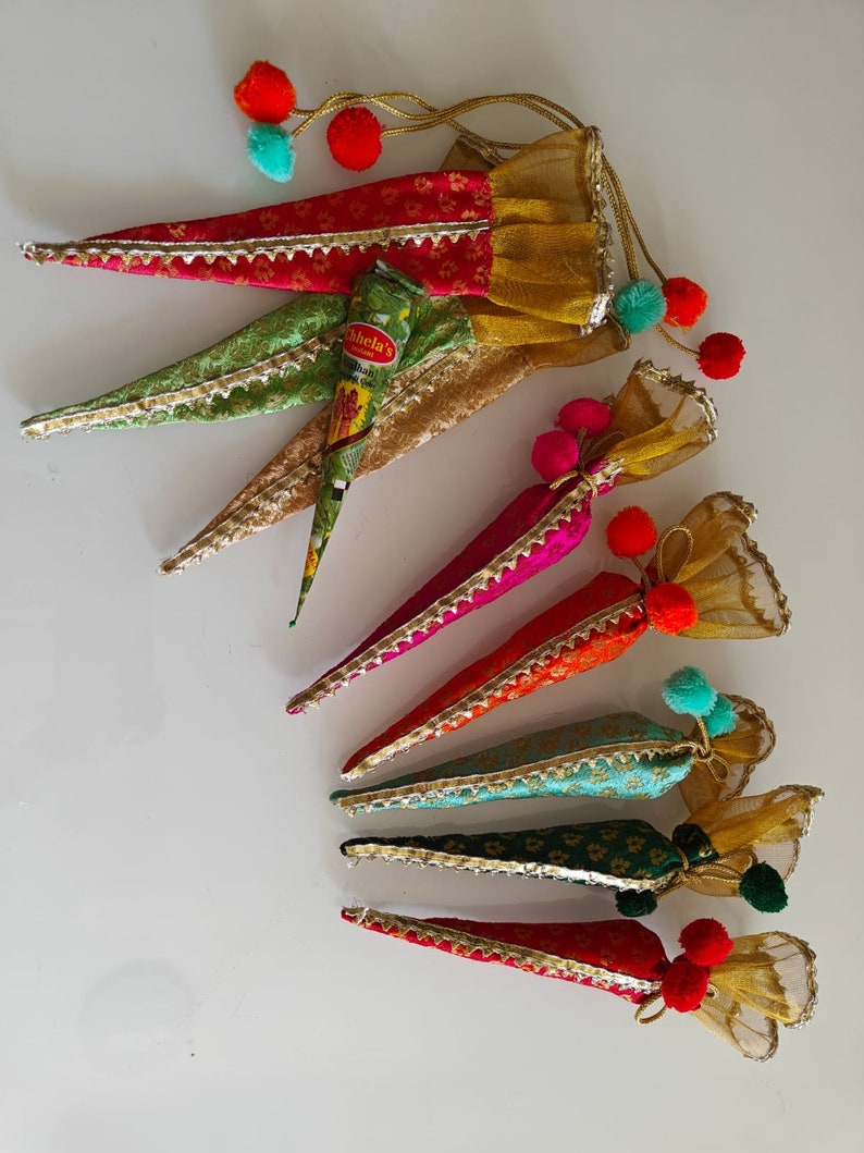 May include: Set of six colorful cone-shaped pouches with gold trim and pom-poms. Each pouch is made of fabric and has a sheer overlay. The pouches are arranged in a row, with the largest pouch at the top and the smallest pouch at the bottom. The pouches are filled with henna paste.