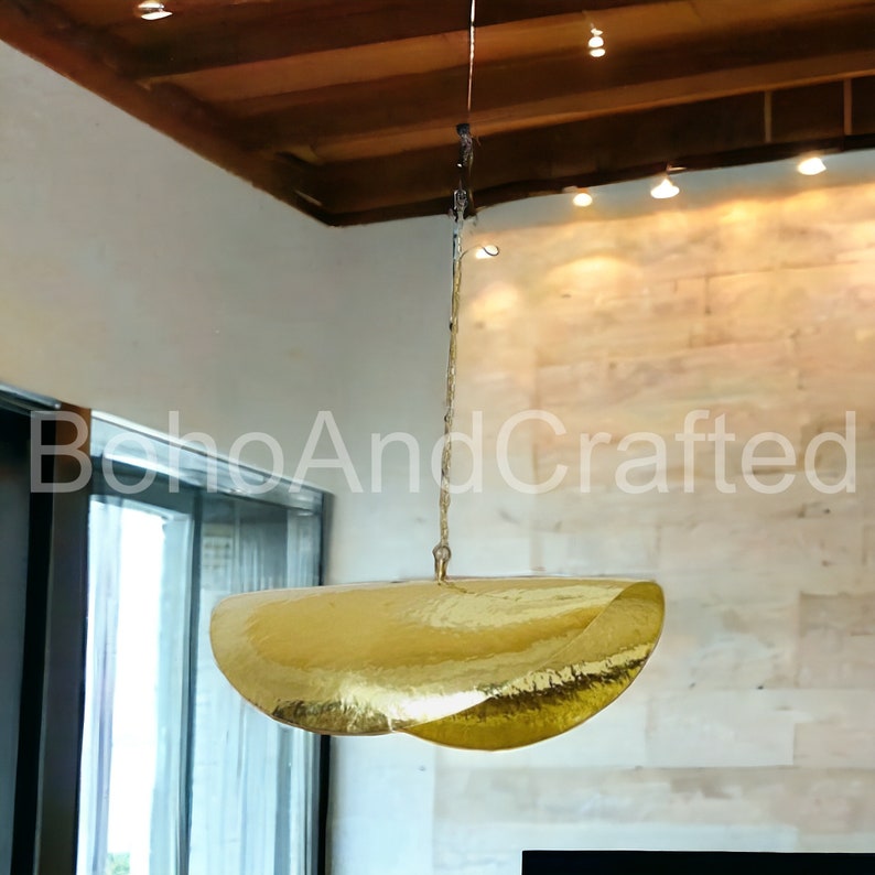 May include: A gold-toned, hammered metal pendant light fixture hangs from the ceiling. The light fixture is shaped like a large, curved, open bowl.