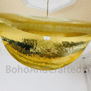 May include: A large, gold, hammered metal pendant light fixture hangs from the ceiling. The light fixture is shaped like a crescent moon and has a smooth, reflective surface.